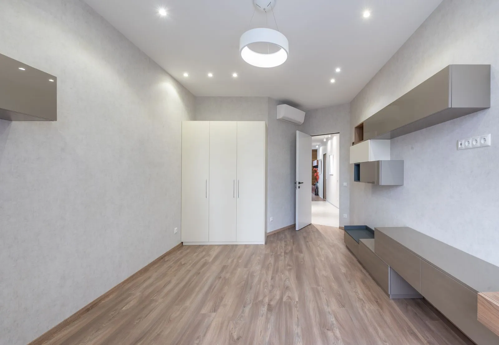 Interior of spacious light room with bright lamps and white wardrobe placed at wall and modern cabinets near opened door